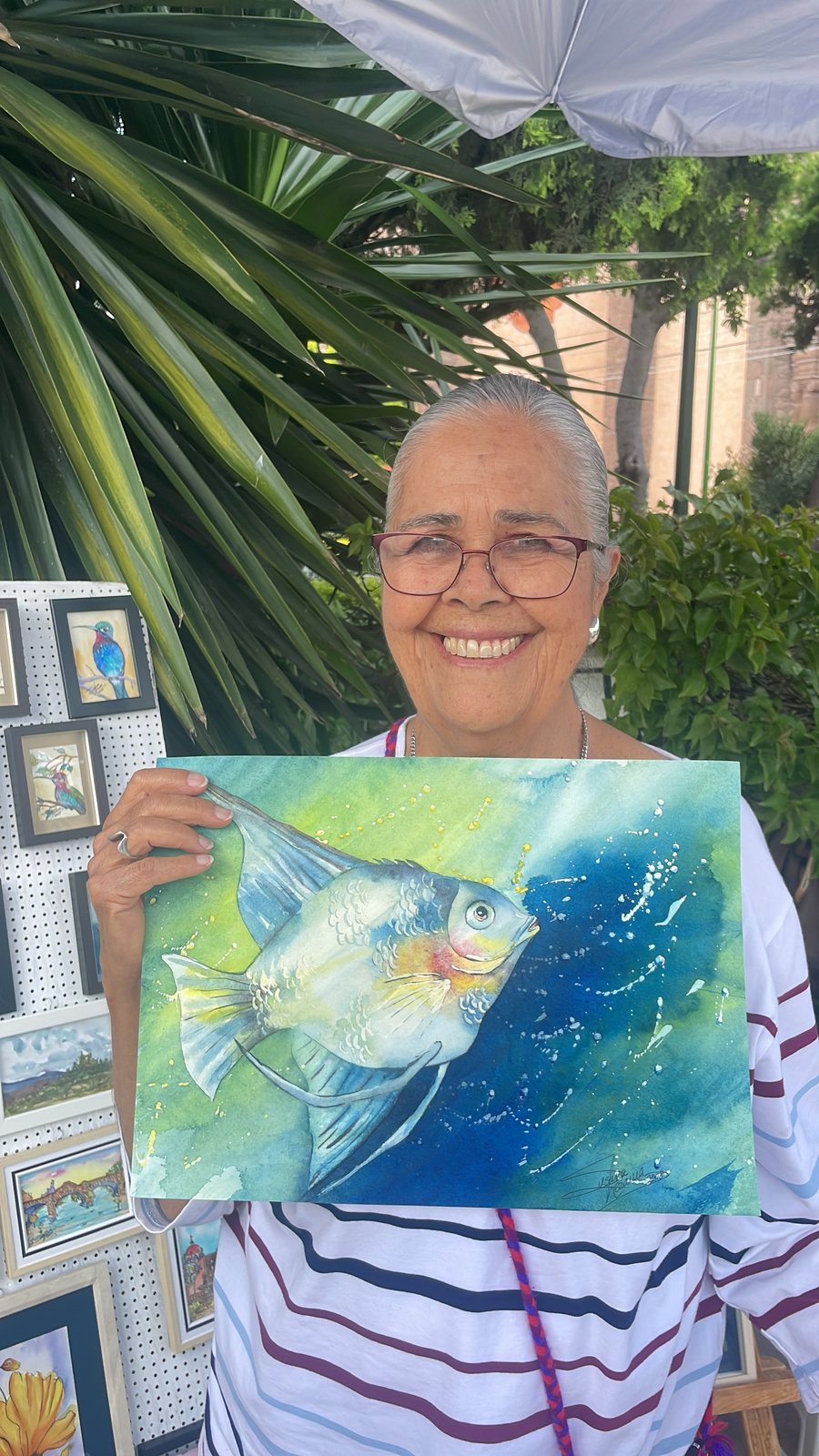 La acuarelista mexicana Susana Lezama en su puesto de arte, sosteniendo su acuarela del pez ángel